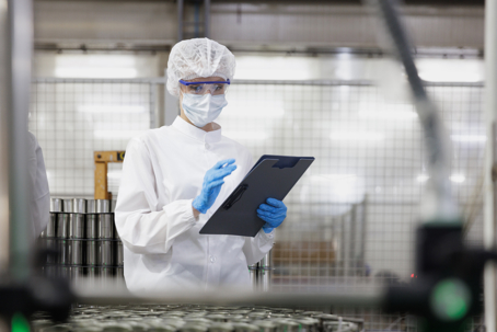 Food safety inspector in protective gear examining produce samples in a clean, modern food processing facility.